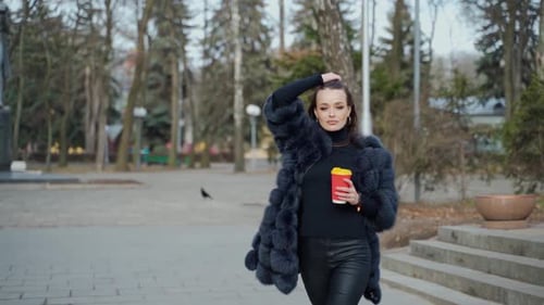 Beautiful young girl in luxury fur coat in the city park.