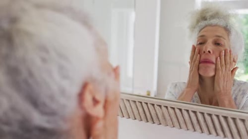 Caucasian senior woman touching her face while looking in the mirror at home