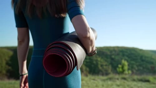 Woman Carries Yoga Mat on Green Hillside