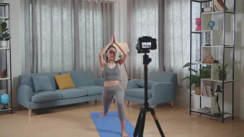 Treinador asiático feminino em roupas esportivas falando para a câmera e fazendo ioga em pose de estocada alta