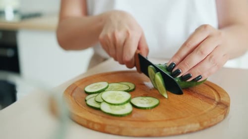 Close-up Slow Motion of Female Hands Cutting Cucumber with Knife in Kitchen