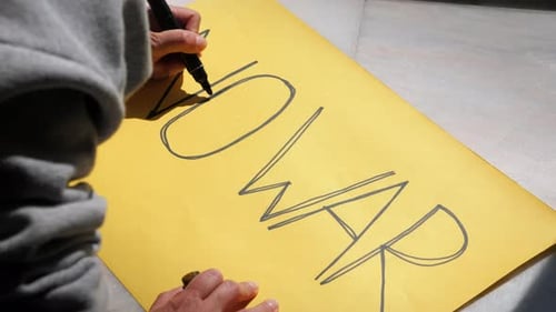 Hand Writing 'No War' Sign on Yellow Paper