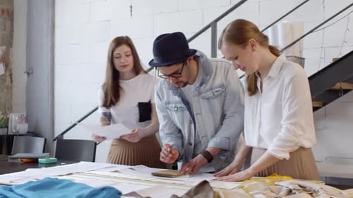 Group of Dressmakers Discussing Fashion Illustrations in Sewing Studio