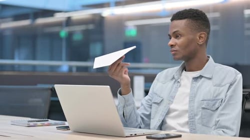 Young Man Plays with Paper Airplane at Desk