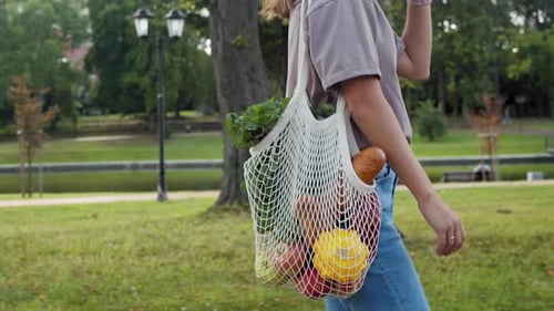 Mujer camina afuera con bolsa de compras de punto de malla