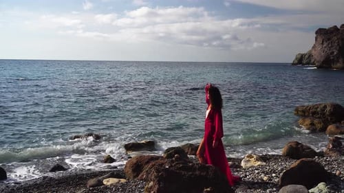 Side View a Young Beautiful Sensual Woman in a Red Long Dress Posing on a Rock High Above the Sea