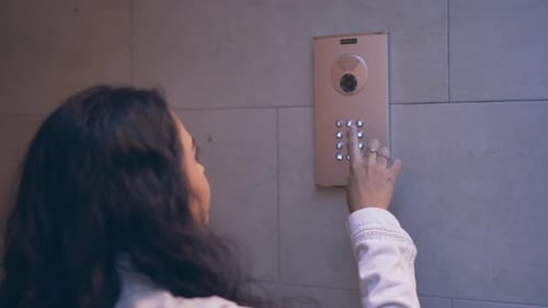 Woman Using Intercom on Building Wall