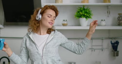 Woman Dances with Headphones and Mug in Kitchen