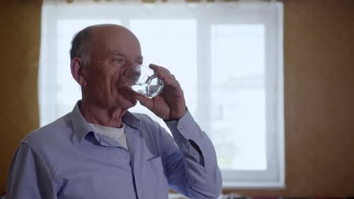 Porträt eines attraktiven alten Mannes, der Durst löscht, trinkt kühles, klares Wasser aus dem Glasbecher lächelnd
