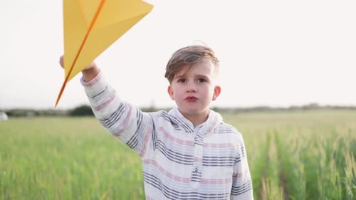 Boy Holding Paper Airplane in Grassy Field