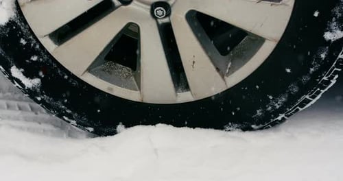 Car tyre moving on snow during snowfall