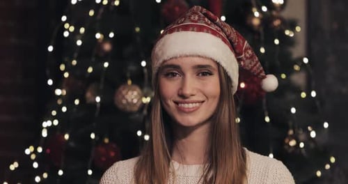 Smiling Woman Wearing Santa Hat in Front of Christmas Tree