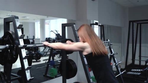 Slender Woman in Sportswear Comes to the Weight Bar and Lifts it in the Gym Near the Mirror