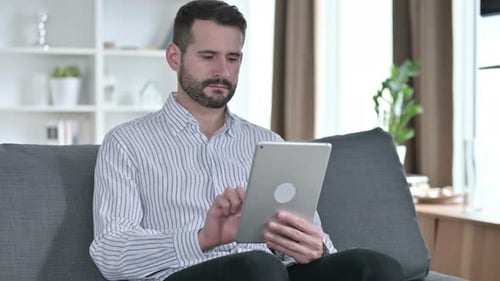 Young Adult Man Using Tablet While Sitting on Couch