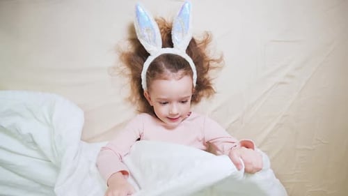 Child in Bunny Ears Hiding Under Duvet