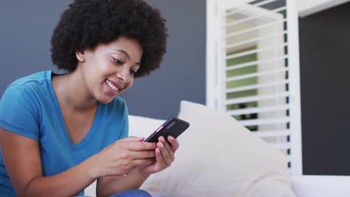 Woman Smiling Using Smartphone While Sitting on Sofa