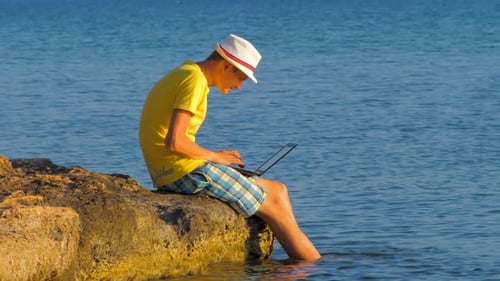 Young Adult Using Laptop On Rocky Beach