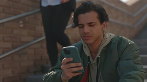 Young Man Uses Cellphone Sitting on Steps