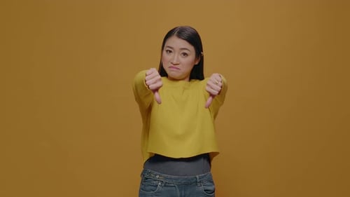 Displeased Woman Showing Thumbs Down on Camera in Studio