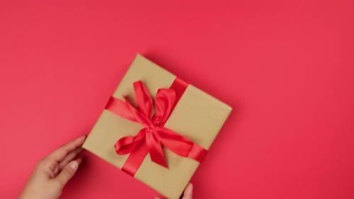 Hands Place Wrapped Gift Box on Red Surface