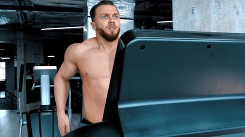 An Attractive Young Man Bodybuilder Running on the Treadmill with an Effort in the Modern Gym