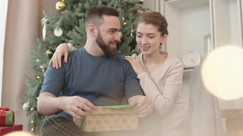 Smiling Couple Opening Christmas Present Together at Home