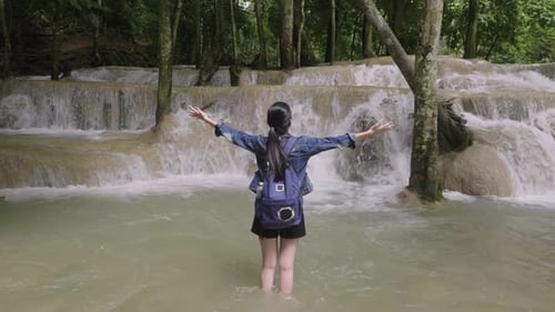 Woman Standing In The River With Her Raised Hands To Waterfall