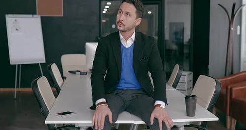 Business Man in the Office Sits on the Edge of the Table