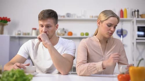 Young Couple Sitting Silently in Kitchen After Argument, Crisis in Relationship