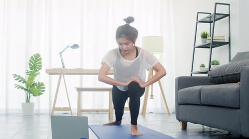 Una jovencita hace ejercicio y usa el ordenador portátil para ver un vídeo tutorial de yoga en casa.