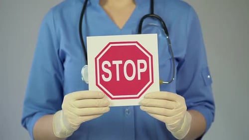 Medical Worker Holding Stop Sign in Hospital Setting