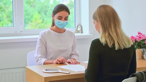 Woman Discussing Document with Masked Medical Professional