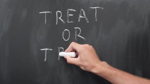 Hand Writes 'Treat or Trick' on Blackboard