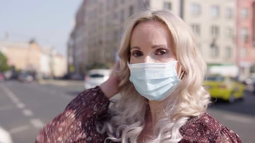 A Middleaged Caucasian Woman in a Face Mask Looks at the Camera in an Urban Area Closeup