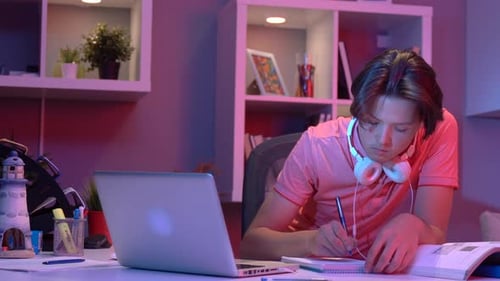 Young Adult Studying with Laptop and Notebook at Night