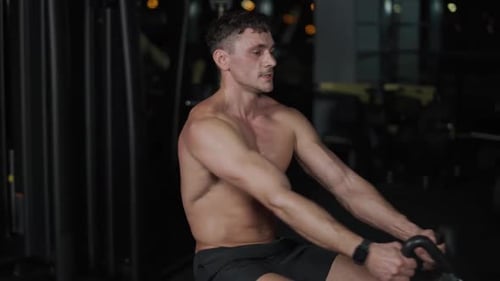 Man in the Gym Lifting Blocks on Rowing Machine Back View Training on Block Device and Gym Equipment