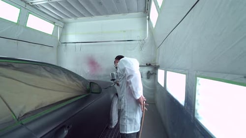 Car body painter spraying car in paint booth