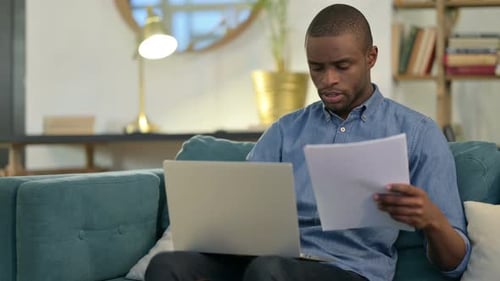 Man Working on Laptop with Document at Home