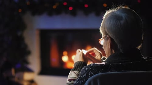 Senior Woman Knitting by Fireplace at Christmas