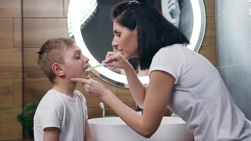 Mother Helping Boy Brush Teeth in Bathroom