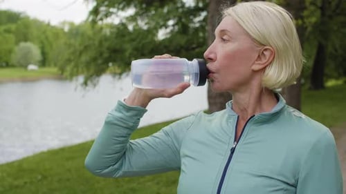 Woman Drinking Water after Exercise in Park