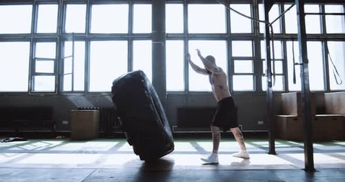 Extreme Workout Muskulöser junger Mann ohne Hemd trainiert mit Riesenreifen während des Trainings im Fitnessstudio