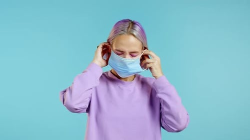 Young Pretty Teenager Girl Puts on Face Medical Mask During Coronavirus Pandemic. Portrait on Blue