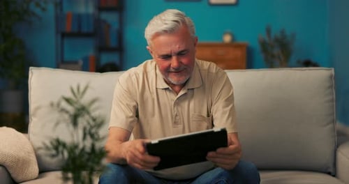 Mature Man Using Tablet Device Indoors on Couch