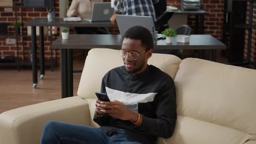 Man Using Phone on Couch in Office Setting