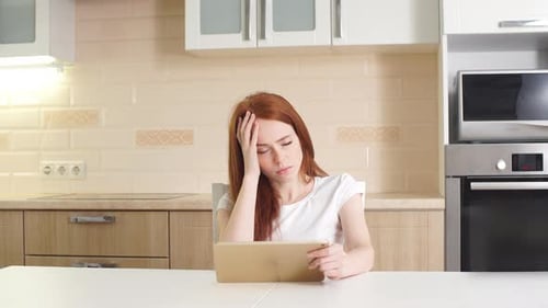 Worried Woman Using Tablet in Kitchen