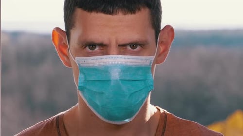 Young Man in a Medical Protective Face Mask Looking at the Camera on the Street Background
