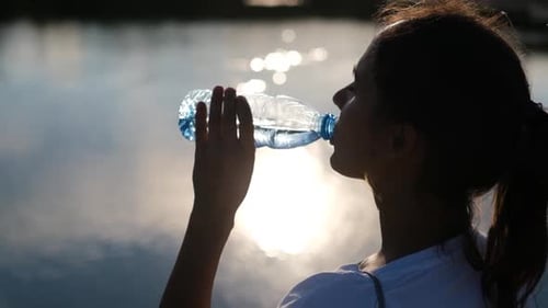 Young Woman Drinking Water by Reflective Lake