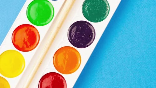 School Set of Children's Paints on a Pastel Blue Background with a Wooden Brush