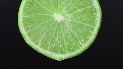 Water drop falling from green hue lime on black background. Lime slice and water splashing, drops